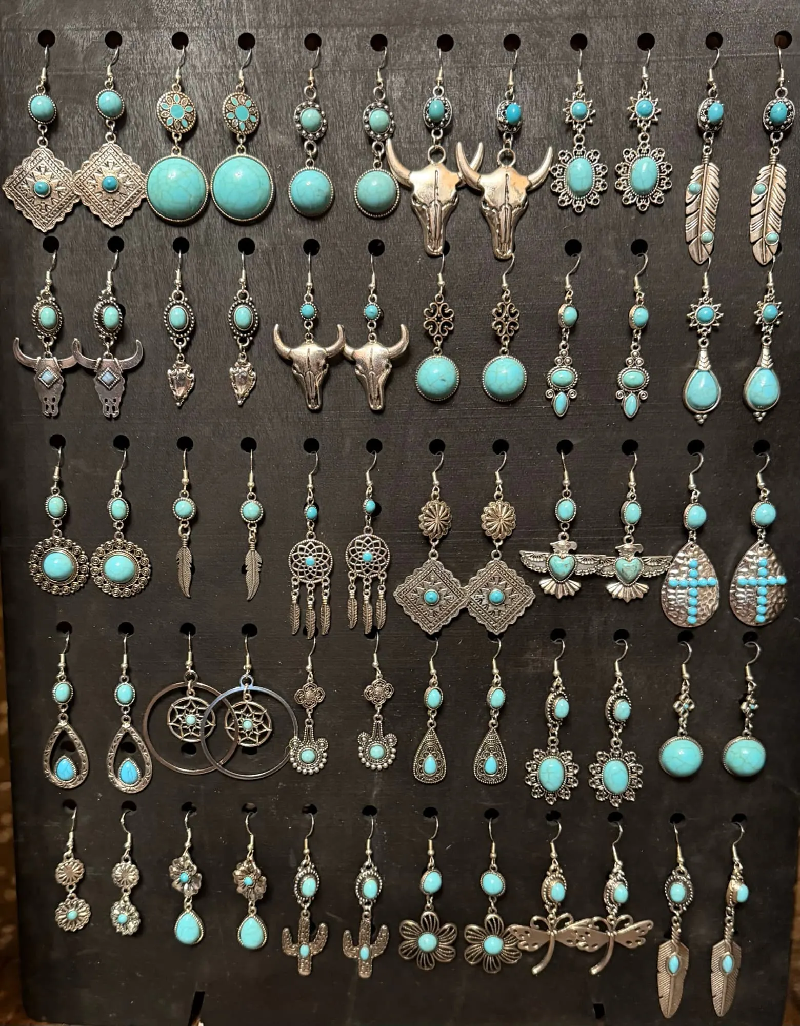 A black board of silver-tone and turquoise earrings: bull skulls, conchos, feathers, thunderbirds, crosses, dreamcatchers, cacti and dragonflies