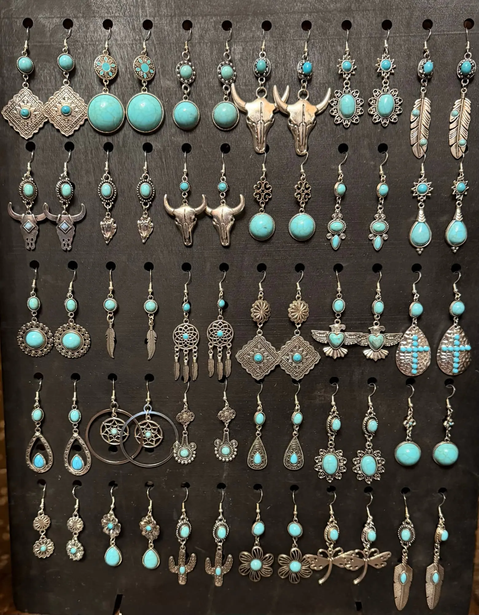 A black board of silver-tone and turquoise earrings: bull skulls, conchos, feathers, thunderbirds, crosses, dreamcatchers, cacti and dragonflies