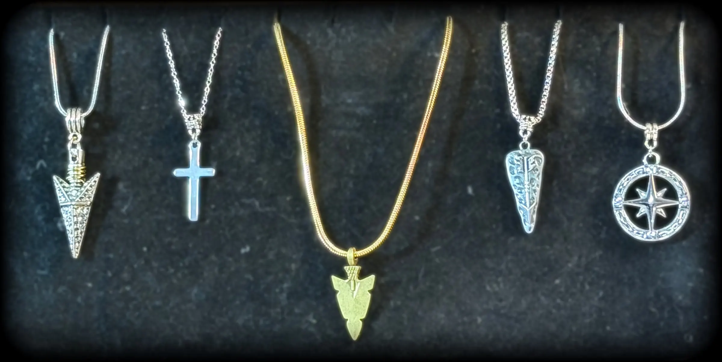Five pendants: a silver arrowhead, a simple cross, a gold arrowhead, a tooled arrow charm and a compass rose