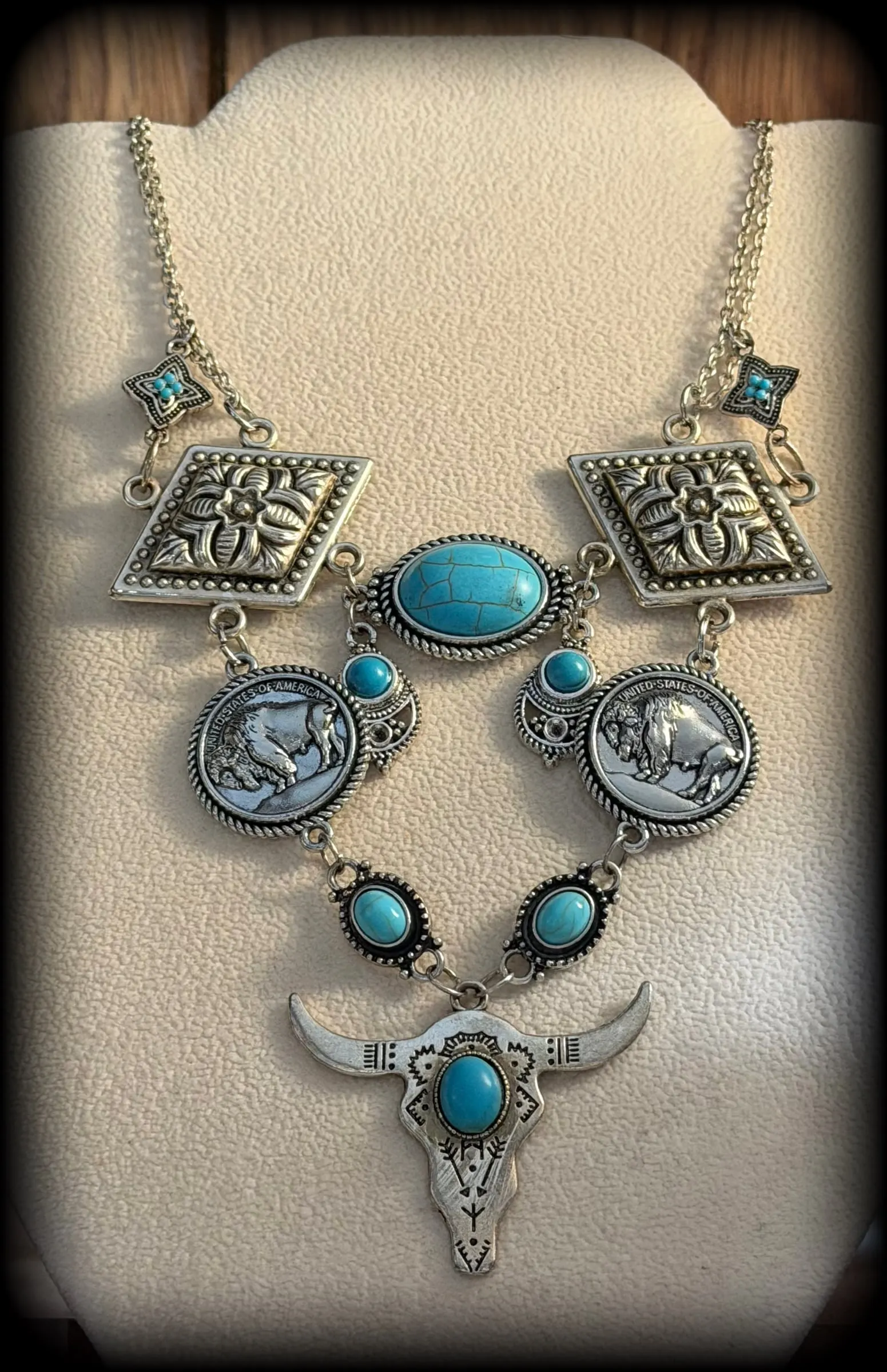 A statement necklace with turquoise conchos, buffalo medallions and a bull skull drop on a cream display bust