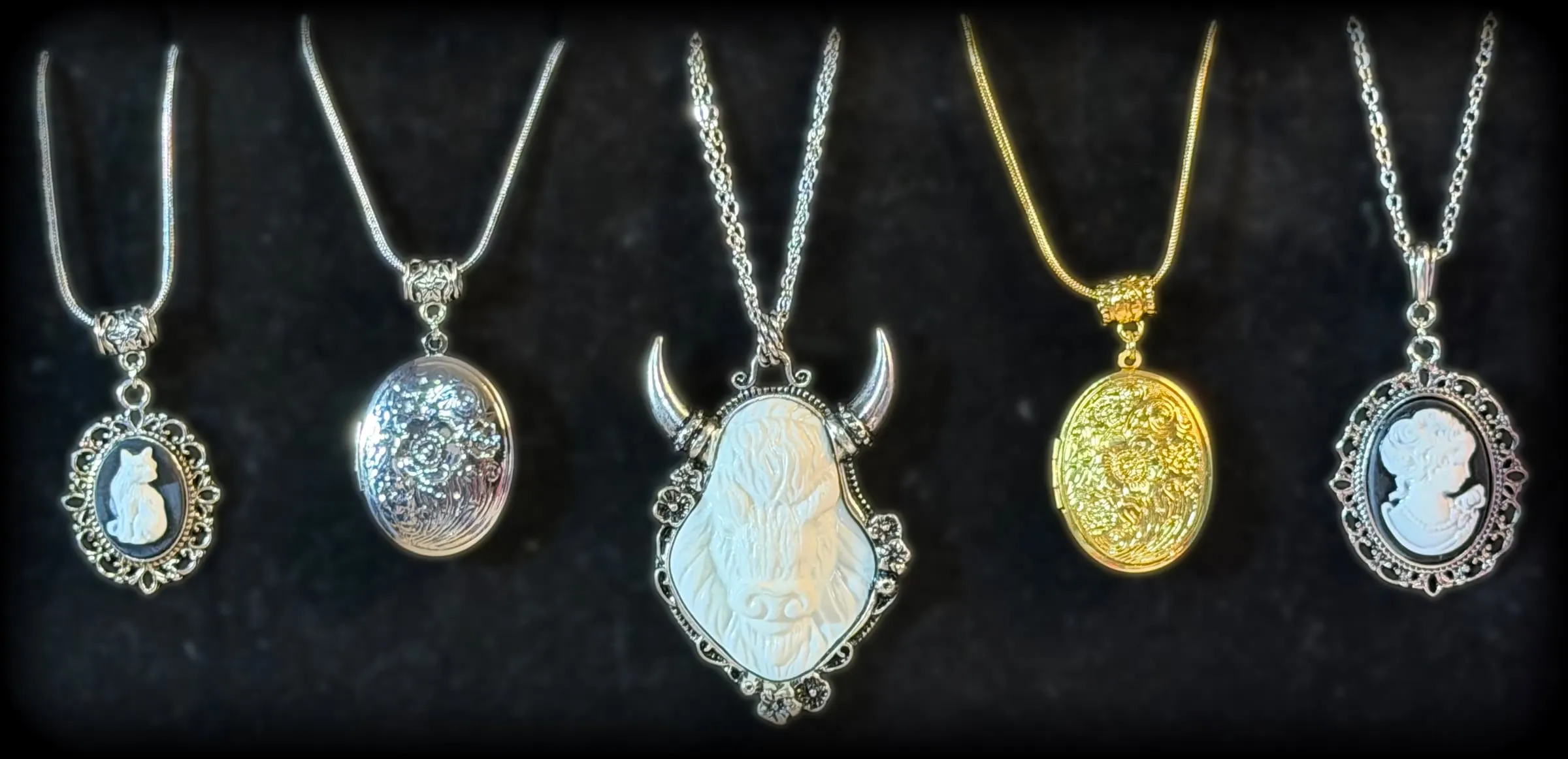 Five pendants: a cat cameo, a silver floral locket, a carved buffalo, a gold floral locket and a lady cameo