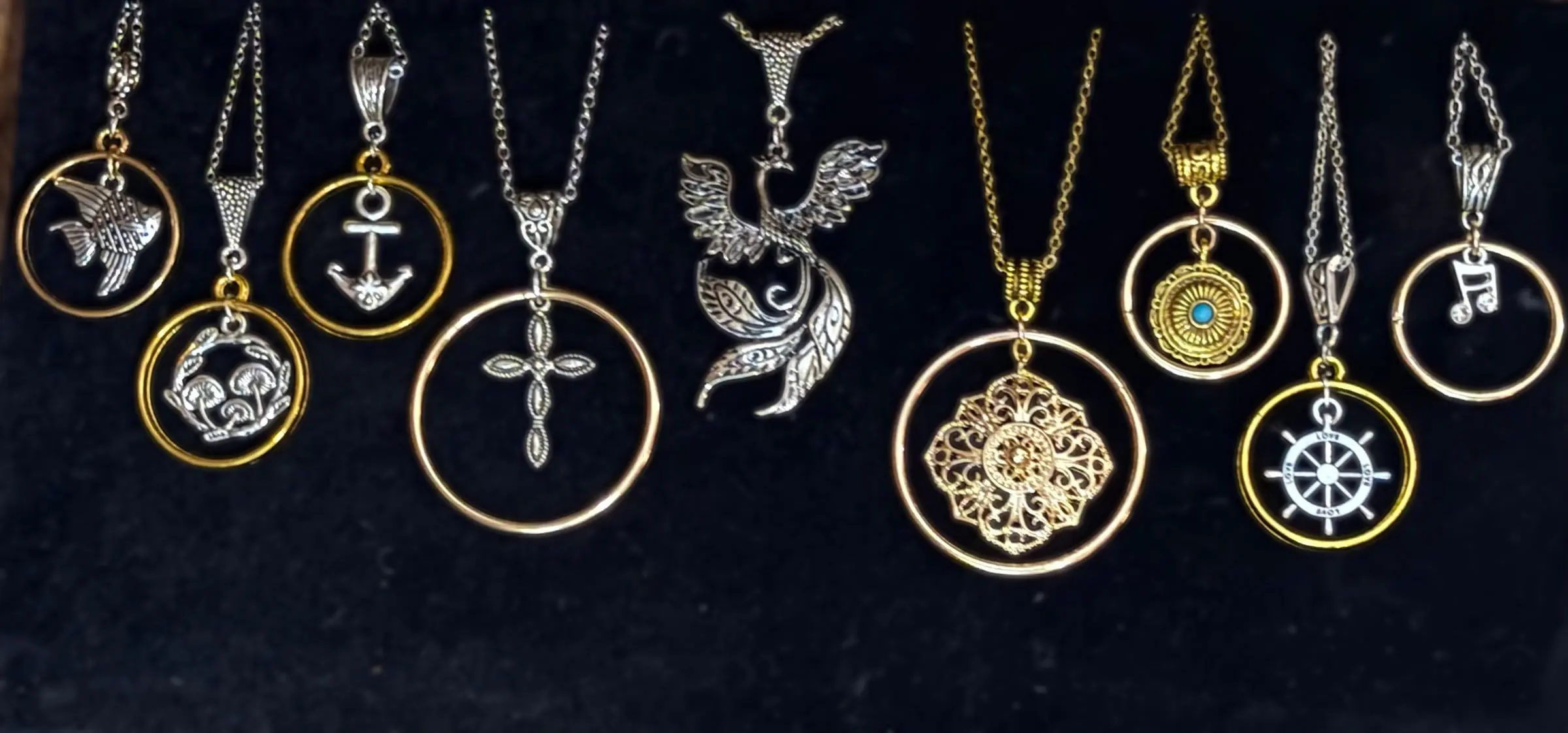 Nine halo pendants: an angelfish, mushrooms, an anchor, a beaded cross, a phoenix, a gold filigree, a turquoise sun, a ship wheel and a music note