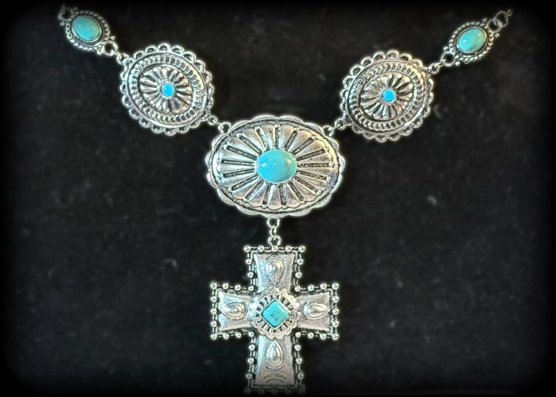 A statement necklace of turquoise conchos with a tooled silver cross drop