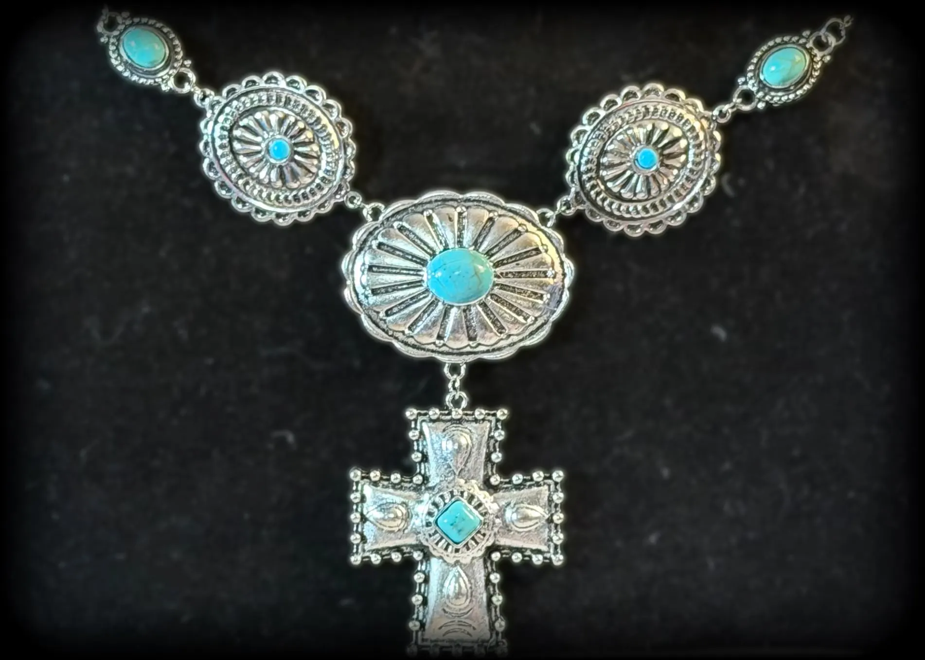 A statement necklace of turquoise conchos with a tooled silver cross drop