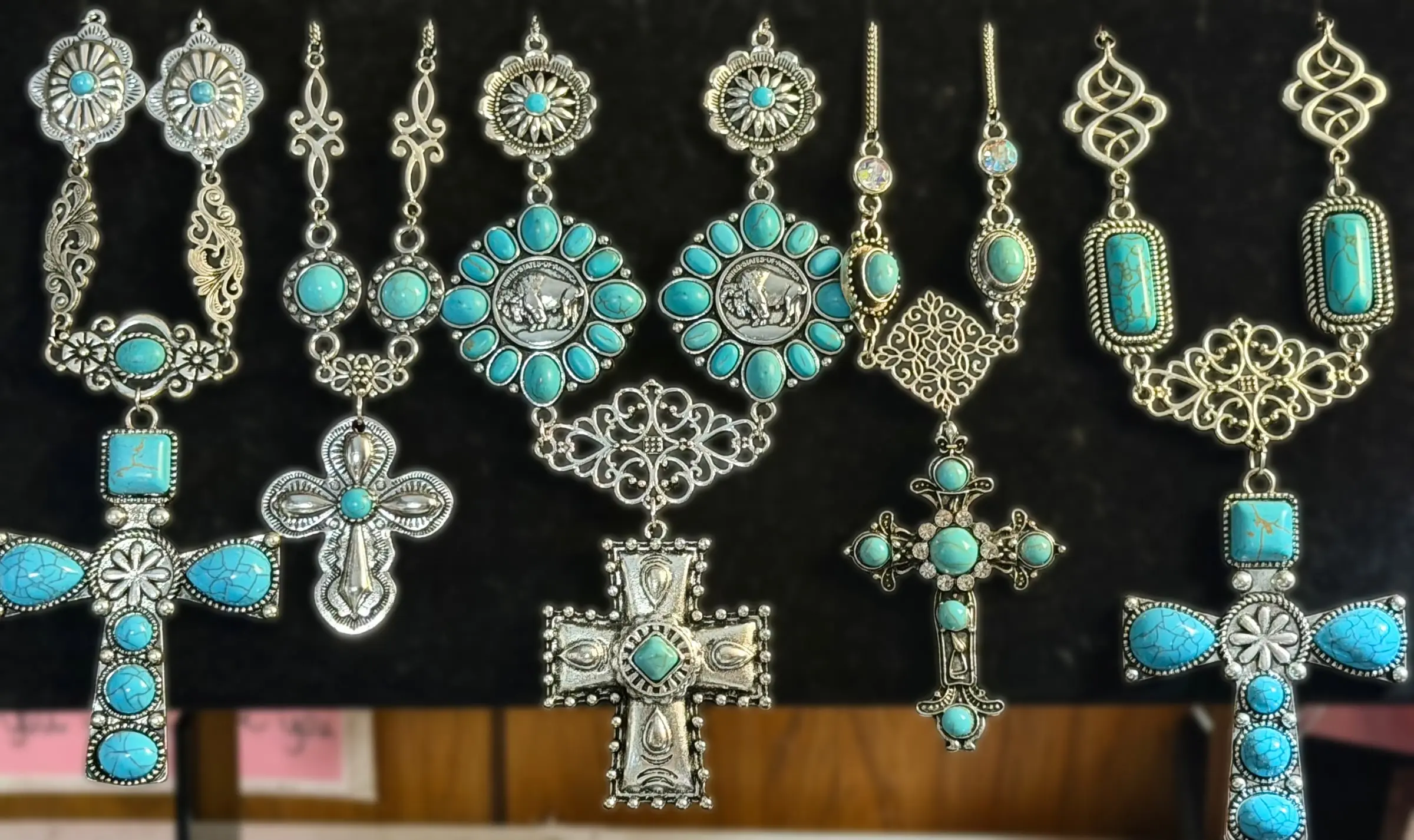 Five turquoise and silver statement cross necklaces on a velvet board, including a buffalo-nickel cross
