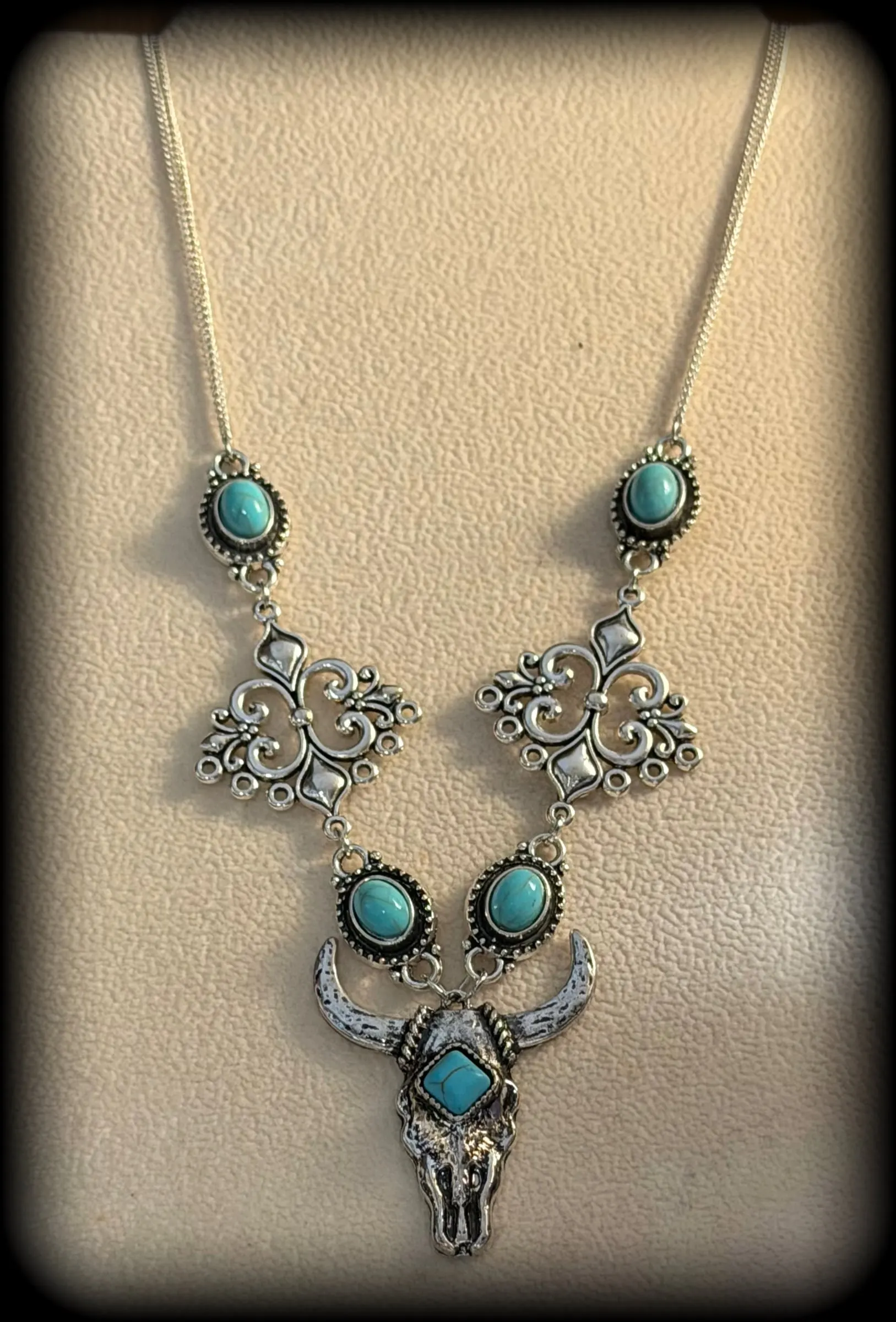 A filigree necklace with turquoise stones and a bull skull pendant on a cream display bust