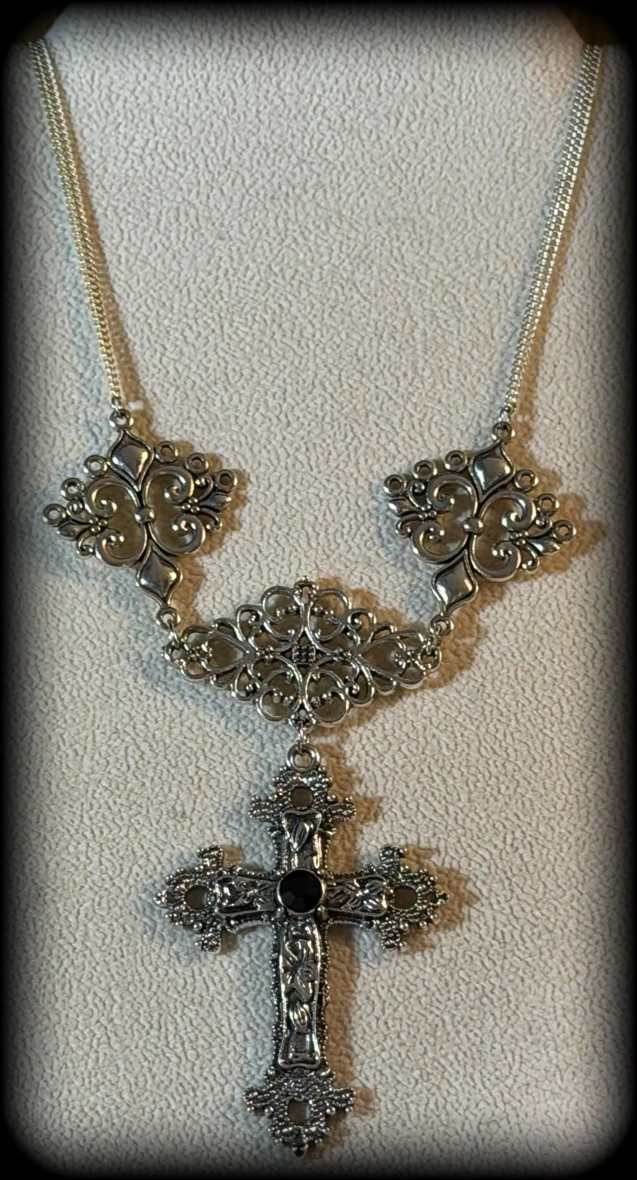 A filigree statement necklace with an ornate silver cross set with a black stone