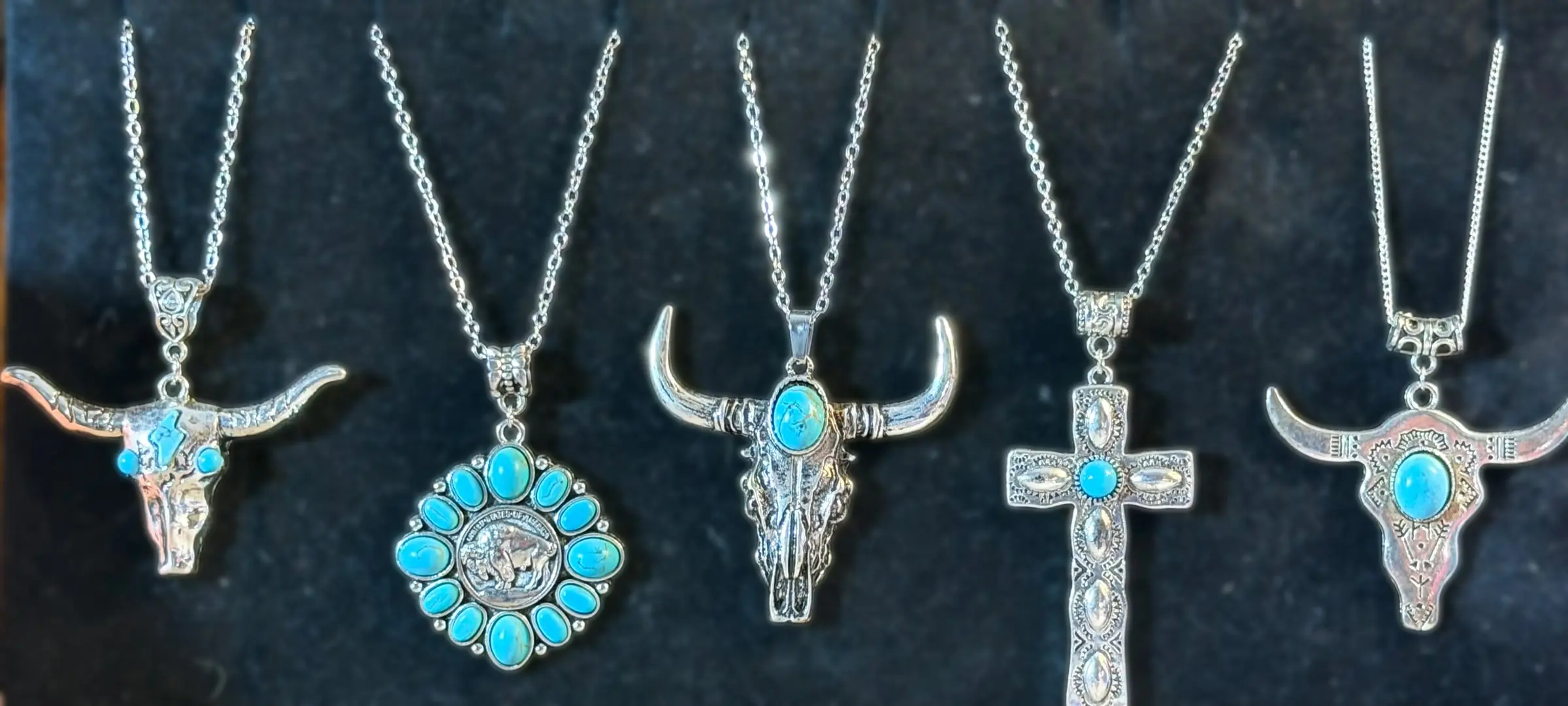 Five western pendants: a turquoise longhorn, a buffalo-nickel blossom, a turquoise bull skull, a tooled cross and an etched bull skull