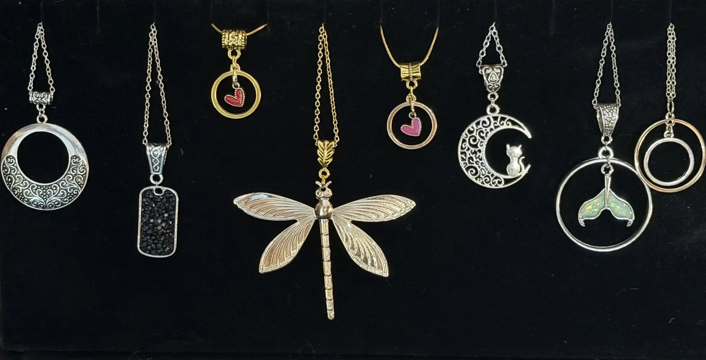 Eight pendants: a scroll hoop, a black crystal tag, two heart halos, a gold dragonfly, a crescent moon with a cat, a mermaid tail and a double ring