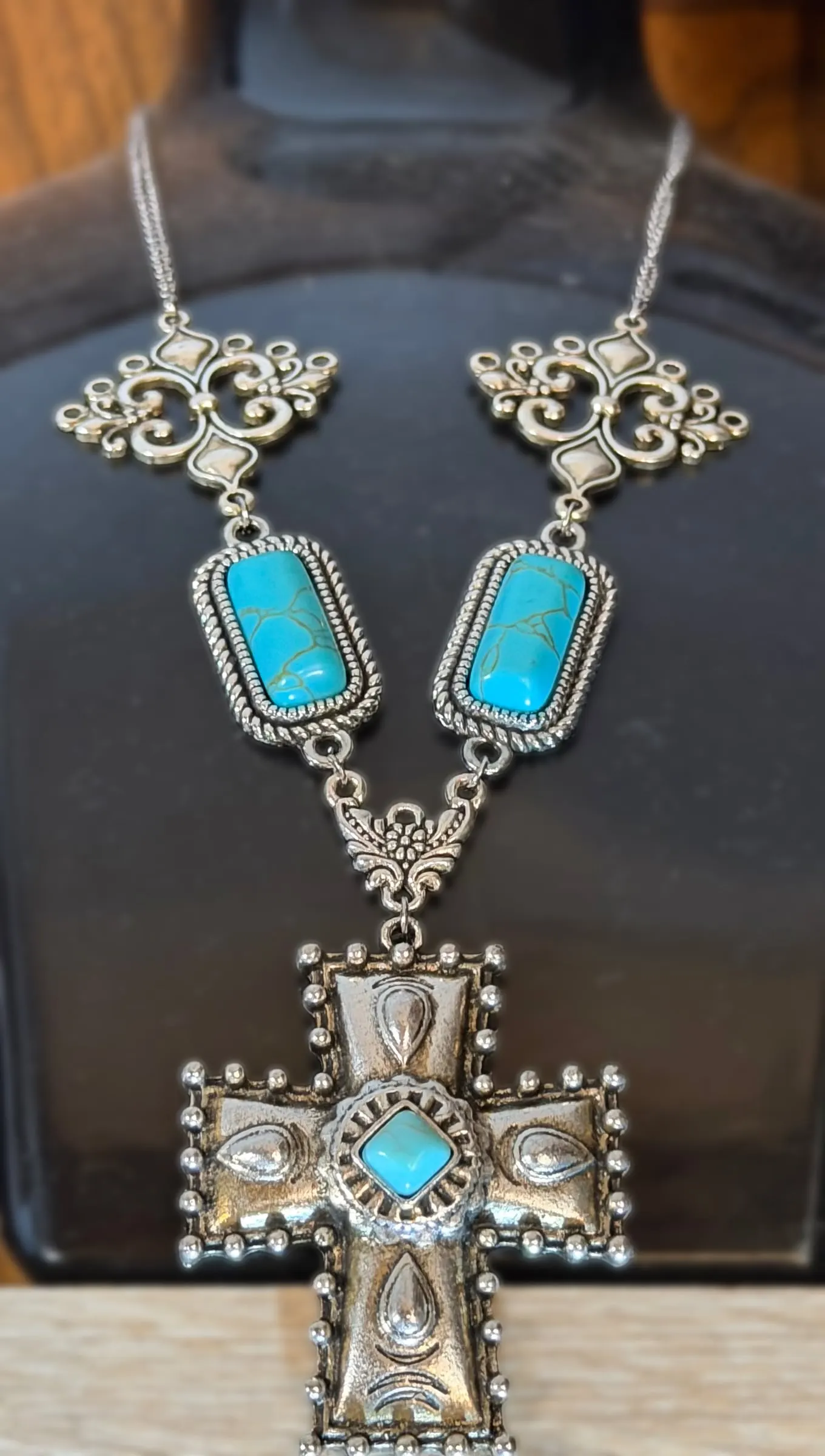 A necklace with turquoise bars, scroll links and a tooled silver cross with a turquoise center