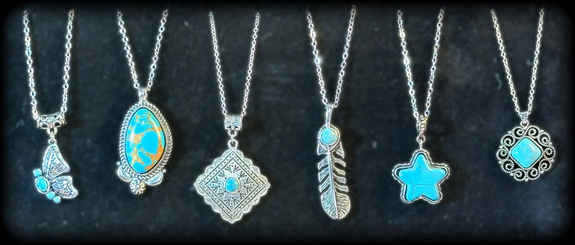 Six silver pendants on black velvet: a turquoise butterfly, a turquoise matrix oval, an etched diamond concho, a feather, a turquoise star and a scrolled square