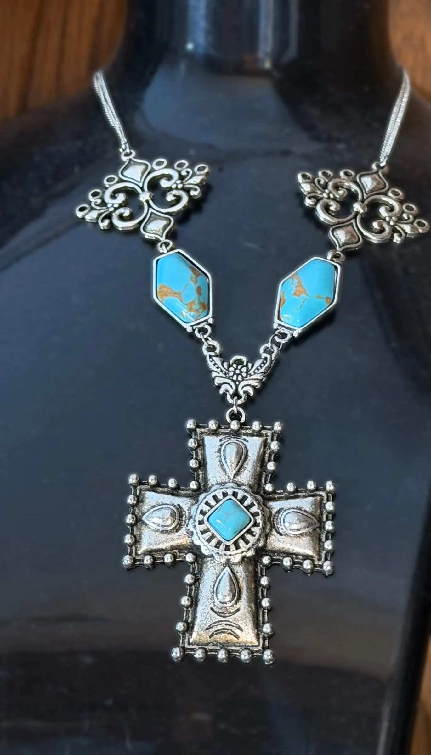 A necklace with turquoise diamond links and a tooled silver cross with a turquoise center