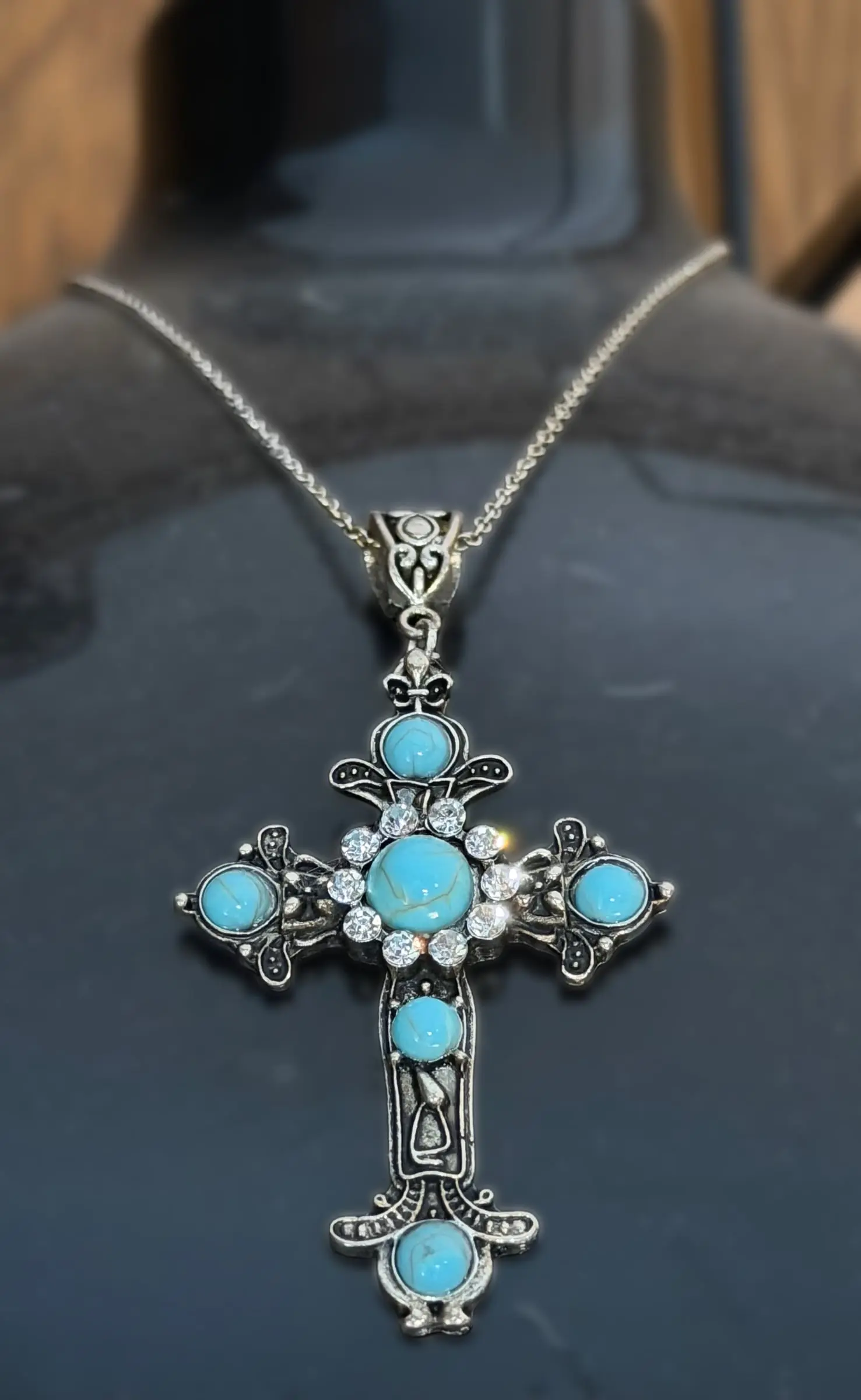 An ornate silver cross pendant set with turquoise stones on a black display