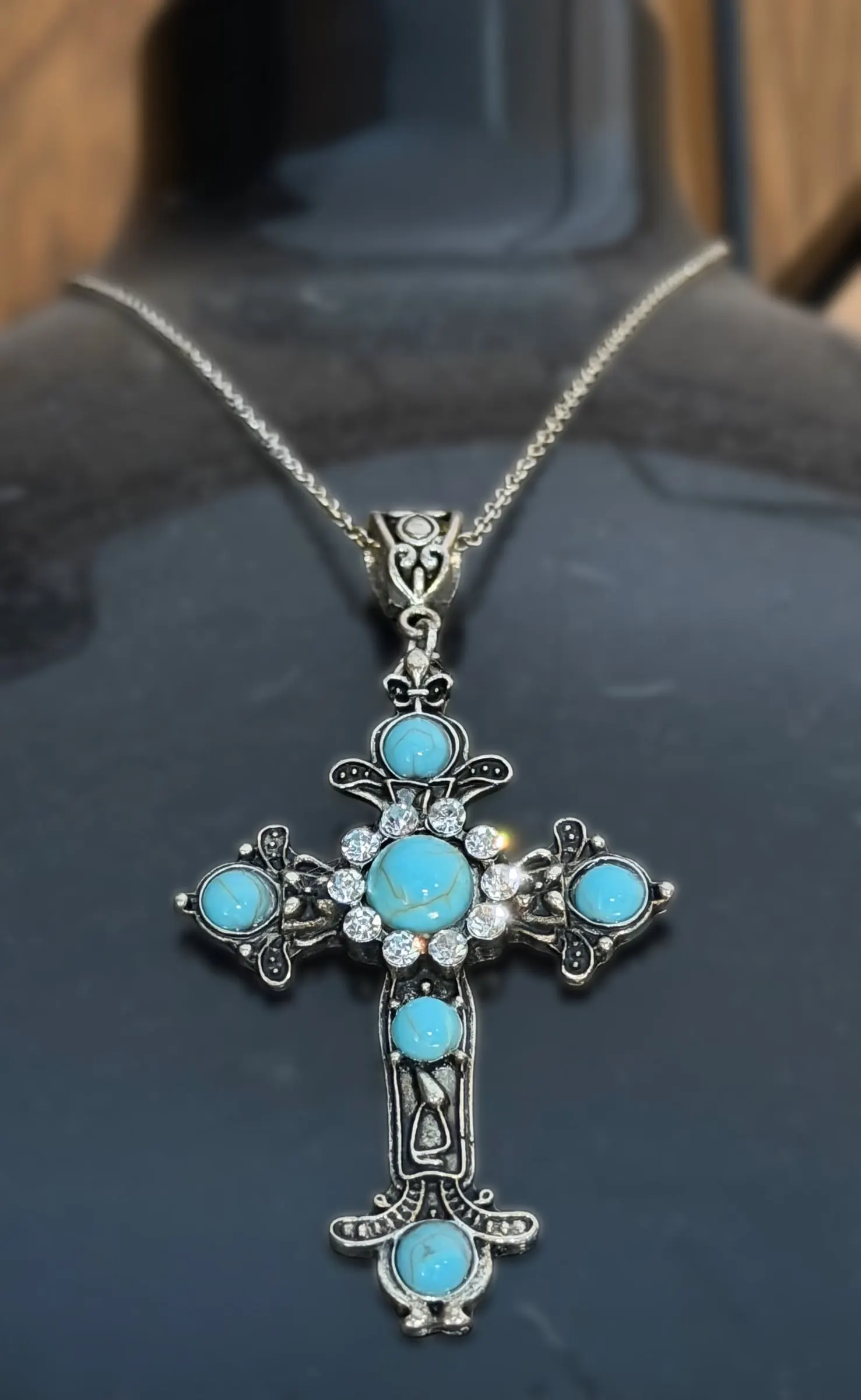 An ornate silver cross pendant set with turquoise stones on a black display