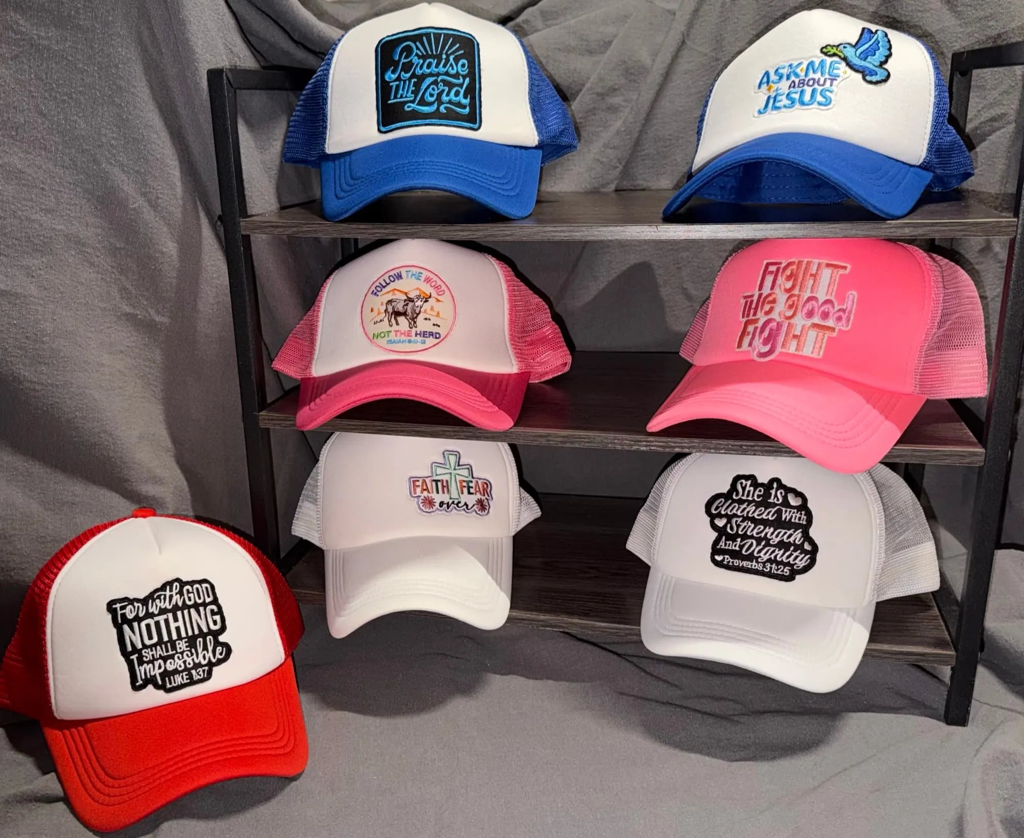 Seven faith-themed trucker hats: Praise the Lord, Ask Me About Jesus, Follow the Word Not the Herd, Fight the Good Fight, Faith Over Fear, She Is Clothed With Strength and Dignity, and For With God Nothing Shall Be Impossible